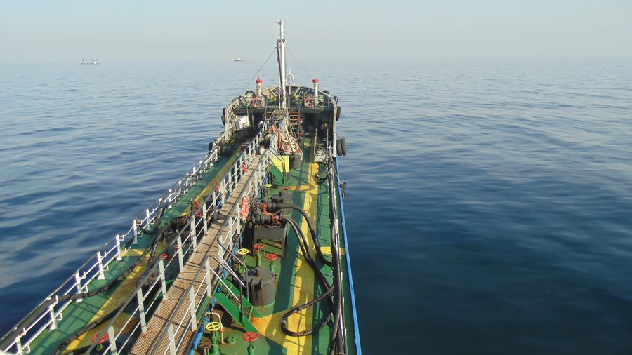Deck of a bunker vessel looking forward along the manifold towards a calm sea.